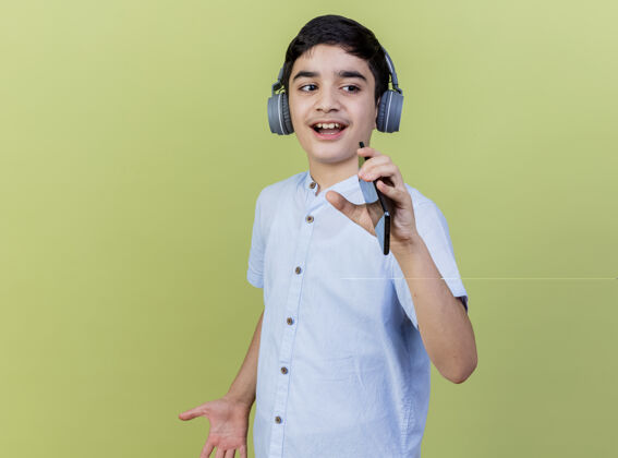 穿着小男孩戴着耳机边唱歌边用手机当麦克风隔离在橄榄绿的墙上人年轻公民