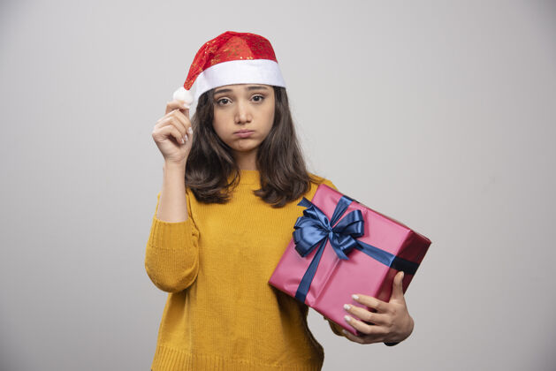 人类一个戴着圣诞老人红帽子 拿着圣诞礼物的心烦意乱的女人人圣诞圣诞老人