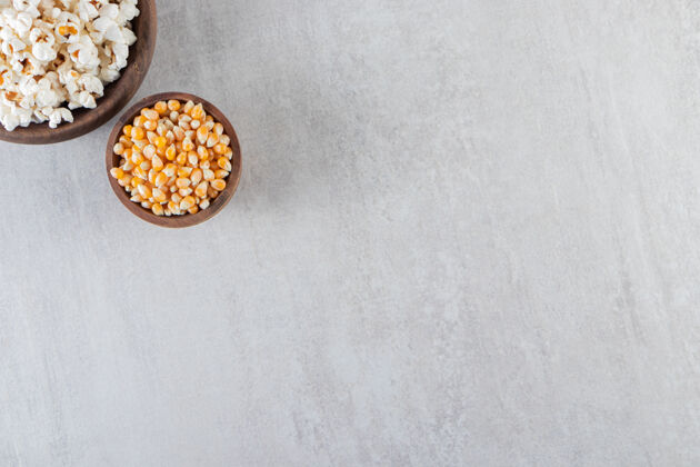 爆米花石桌上放着木碗爆米花和生玉米粒可口背景顶视图