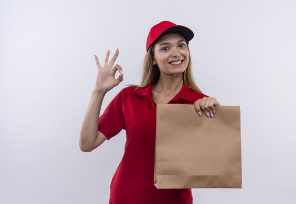 送货面带微笑的年轻送货女孩身穿红色制服 戴着帽子 手里拿着纸袋 脸上露出奥基·格斯鲁尔孤立的白色帽子制服表情