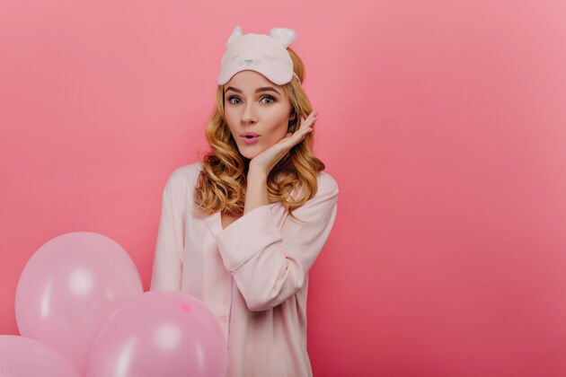 节日惊喜迷人的女人 波浪形的发型 享受着早上的生日漂亮的女孩戴着眼罩 穿着睡衣 手里拿着粉红色的气球惊喜睡衣氦气球