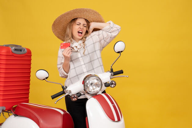 年轻女子俯视图：戴着帽子 坐在摩托车上 拿着银行卡 正在收行李的快乐而情绪激动的年轻女子收集人摩托车