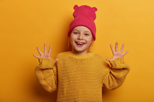 玩积极向上 保持微笑高兴可爱的欧洲孩子举手伸手掌 表达良好的情绪 与人玩耍 穿着针织毛衣 隔离在黄色的墙上宽松室内脸
