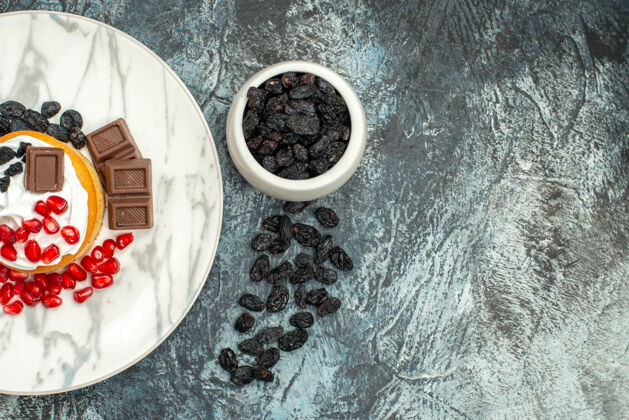 美味的奶油蛋糕顶视图美味的奶油蛋糕与巧克力石榴和葡萄干浅黑色的背景木头饼干派