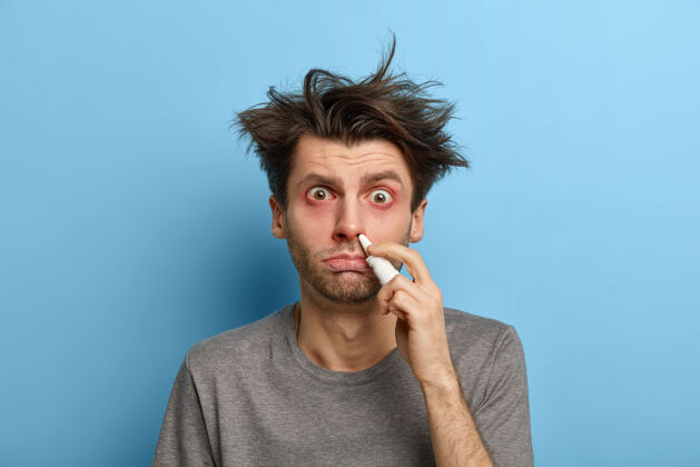 人不健康的头发病患者使用滴鼻剂 治疗感冒症状 眼睛发痒 冬季患鼻炎 隔离在蓝色墙壁上 治疗鼻塞医学概念药物欧洲治疗