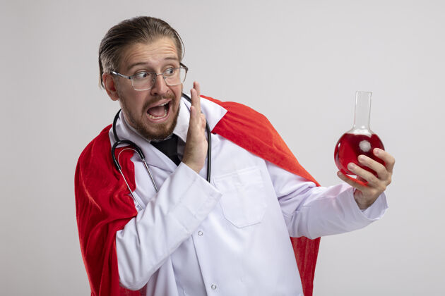 眼镜一个年轻的超级英雄 穿着医用长袍 戴着听诊器和眼镜 手里拿着装满红色液体的化学玻璃瓶 隔离在白色背景上持有长袍玻璃