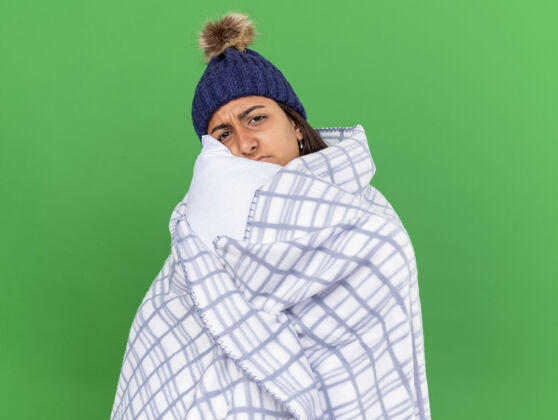 围巾戴着冬天帽子 围巾裹在格子布里的未出嫁的生病少女抱枕 隔离在绿色背景上疾病枕头女孩