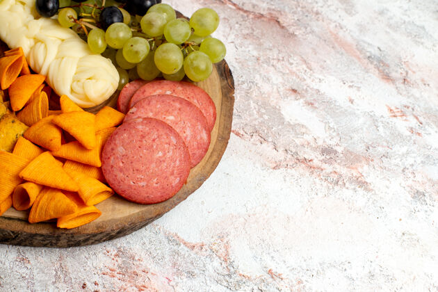 水果前视图不同的小吃cips香肠奶酪和新鲜葡萄在浅白色空间葡萄食品前