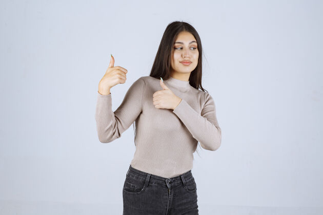 聪明穿灰色衬衫的女孩在做竖起拇指的招牌享受人体模特协议