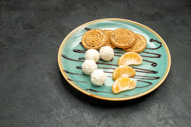 蛋糕前视图甜饼干和椰子糖在深灰色桌子饼干糖果蛋糕盘子里餐椰子小吃