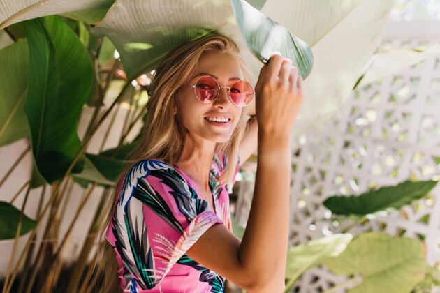 人可爱的长发女人戴着粉色太阳镜在植物旁摆姿势温室年轻背景