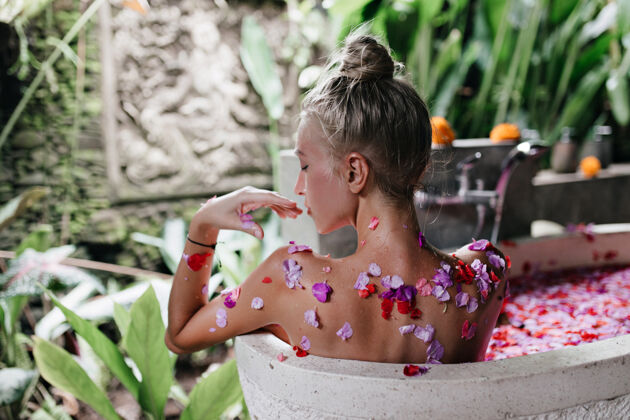 享受高加索女模特在满是花瓣的浴缸里休息美丽的年轻女士在早晨做spa卫生身体护理人