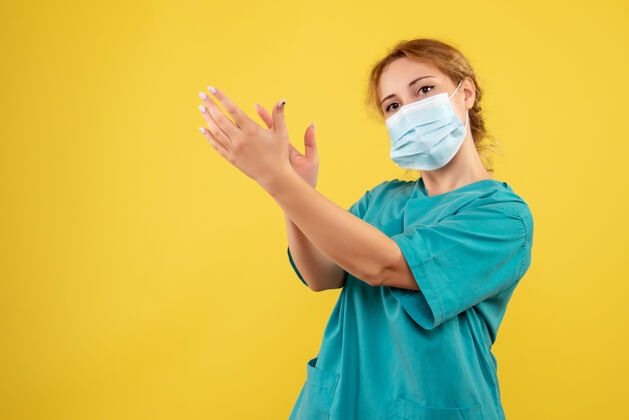 成人身着医疗服 戴着无菌口罩的年轻女医生的正面图在黄色的墙上拍打人人医疗
