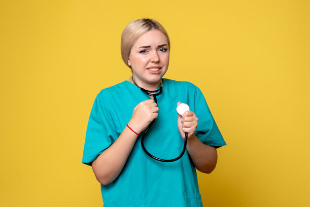 器械黄色墙壁上穿着带听诊器的医用衬衫的女医生的正视图正面医院健康