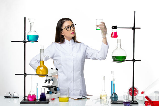 科学前视图：穿着无菌医疗服的女化学家正在用浅白色背景的解决方案研究实验室病毒冠状病毒-大流行科学烧杯化学灭菌