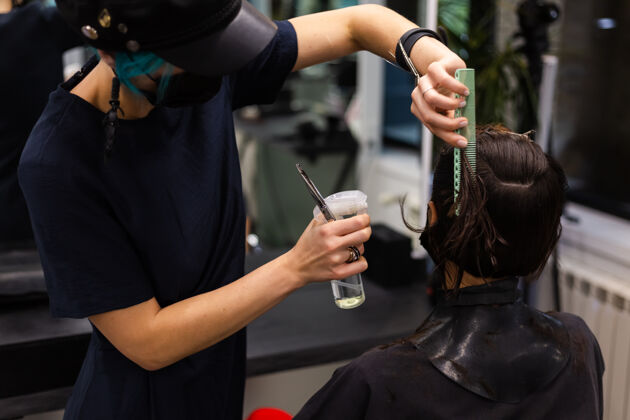 发廊一个专业的女理发师给客户理发这个女孩戴着面具坐在美容院里面部流行工人