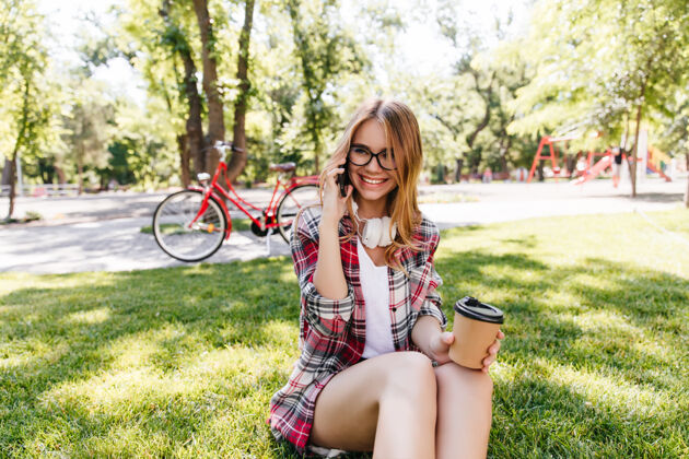 夏天温文尔雅的女孩坐在草地上打电话微笑可爱的女人端着咖啡的户外照片休闲骑人