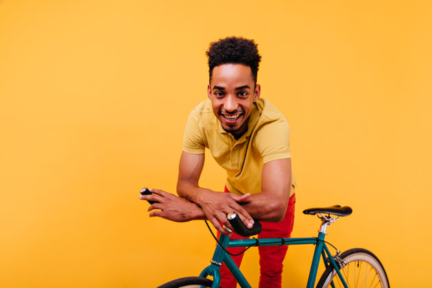 年轻可爱的非洲男人卷发站在自行车旁室内拍摄的狂喜的黑人摆姿势帅气人人