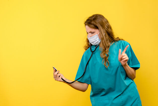 人黄色墙上戴口罩的女医生用听诊器的正面图护士医疗器械听诊器
