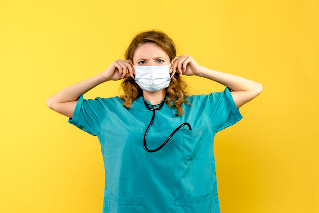 医院黄色墙上戴着无菌口罩的女医生的正视图听诊器绝育器械