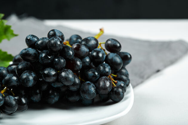 水果白盘子上的黑葡萄叶子和灰色桌布高质量的照片自然叶子桌子
