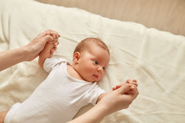 活跃托儿所的妈妈和孩子在做婴儿手臂的练习 孩子看向别处 穿着白色的紧身衣 躺在毯子上 妈妈牵着孩子的手手臂儿子新生儿