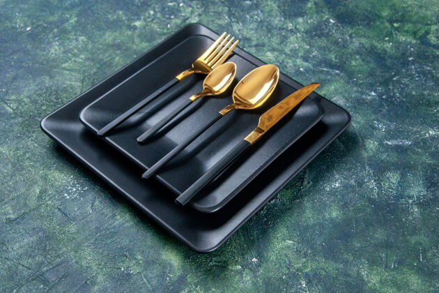 勺子正面图黑色的盘子和金色的勺子叉子和刀子在黑暗的背景上刀金的厨房