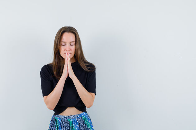 健康年轻女子站在祈祷姿势在黑色t恤和蓝色裙子 看起来轻松皮肤护理完美姿势