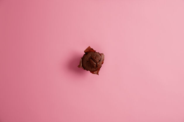 糕点刚刚烤好的美味巧克力松饼 用牛皮纸从上面拍下 隔离在粉色背景上 即食垃圾食品 甜点 热量和营养概念选择性聚焦松饼垃圾蛋糕
