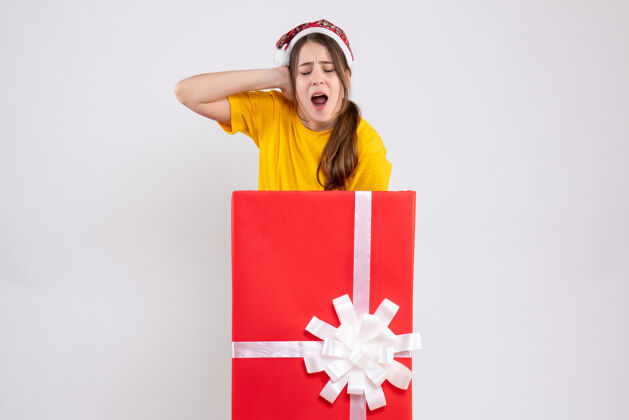 人前视图愤怒的女孩 戴着圣诞帽 站在圣诞礼物后面丝带圣诞节购物