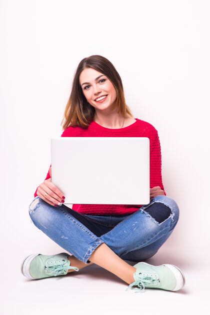 漂亮快乐的年轻女子盘腿坐在地板上 在灰色的墙上用笔记本电脑人地板聊天