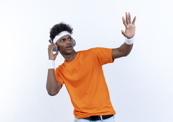 穿着看着身边关心的年轻的美国黑人运动男子戴着头带和腕带和耳机显示停止手势孤立的白色背景运动年轻显示