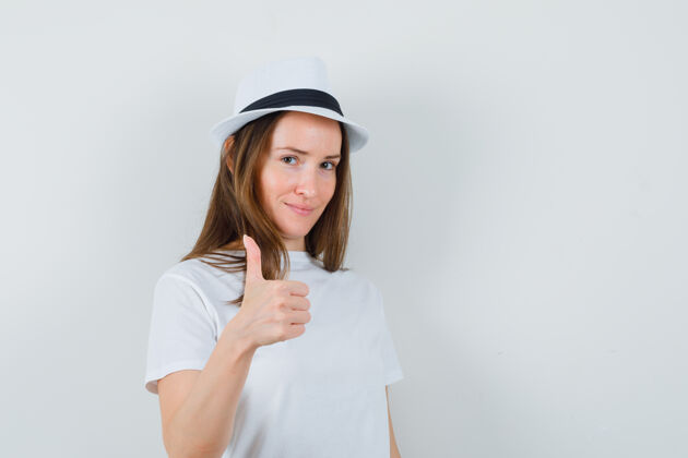 帽子一个戴着白色t恤礼帽的年轻女孩竖起大拇指 看上去很自信女性快乐童年