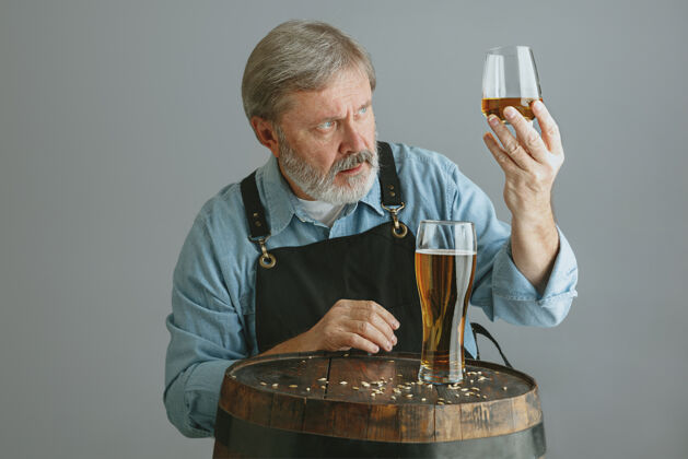 技术自信的高级酿酒师 在灰色的木桶上 用玻璃瓶自制啤酒蒸馏器过程年轻人