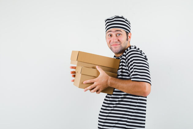 花花公子年轻的男人穿着t恤 戴着帽子 手里拿着纸板箱 看上去很高兴盒子男人帅哥