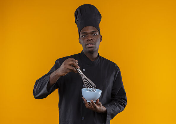 橙色年轻自信的美国黑人厨师身着厨师制服 拿着打蛋器和碗放在橘子上 留有复印空间空间烹饪复制