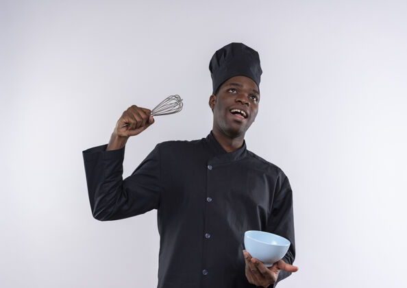 空间年轻快乐的非洲裔美国厨师穿着厨师制服 拿着打蛋器和碗放在白色的空间里举行年轻非裔美国人