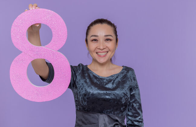 八快乐而积极的亚洲女人拿着纸板做的8号 站在紫色的墙上 面带微笑 兴高采烈地庆祝国际妇女节微笑站立国际