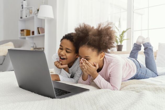 孩子两个微笑的兄弟姐妹在家里一起玩笔记本电脑团结房子室内
