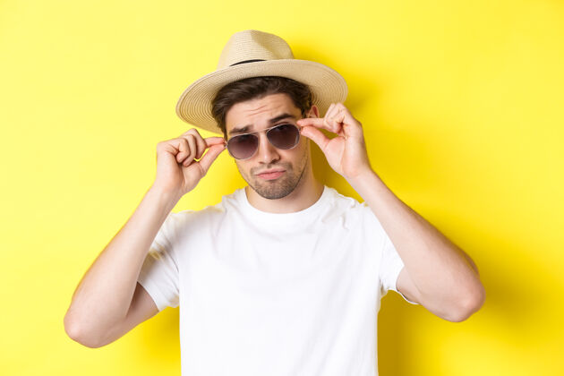 夏天旅游和度假的概念特写凉爽的游客享受假期旅行 戴着草帽 黄色背景太阳镜男人成年人帅气
