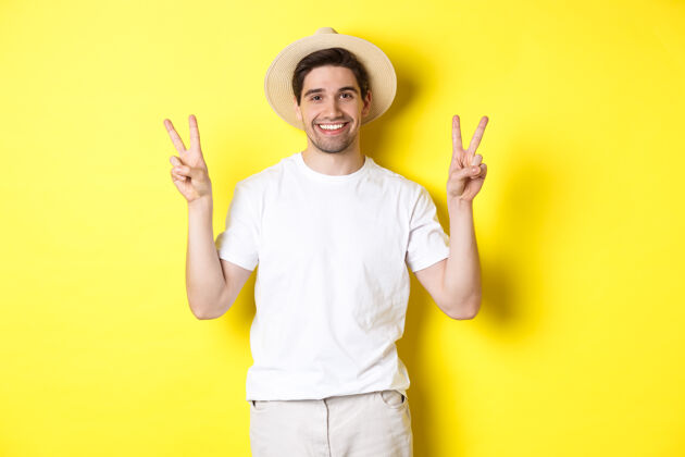 黄色旅游度假的概念快乐的男游客摆出和平的姿势拍照 微笑着兴奋 站在黄色背景下年轻男人模特