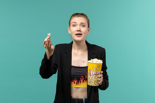 女商人正面图：年轻女性手持爆米花包 在蓝色表面看电影电影剧院年轻女性