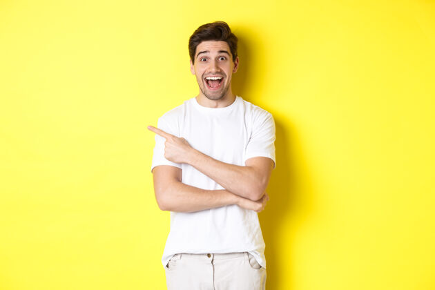 模特快乐的男人指着左边的手指 在广告版面上展示广告 笑容可掬 穿着白衣服站在黄色的背景下秀男人指