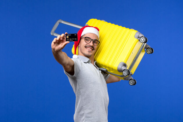 圣诞节正面图：年轻男子手持黄包和银行卡乘坐蓝色背景的度假飞机飞行人男性飞机