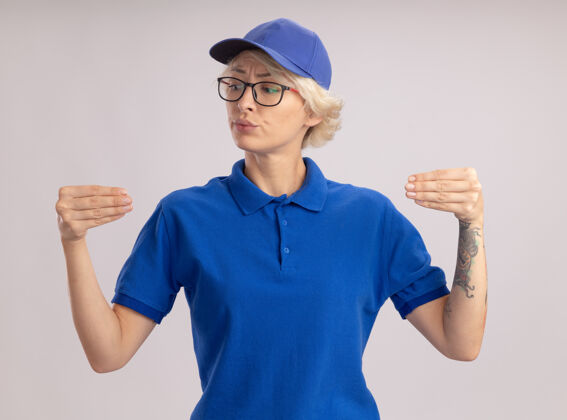 制服身穿蓝色制服 戴着眼镜的年轻送货女自信地用手做着手势 站在白色的墙壁上的肢体语言概念交货眼镜信心