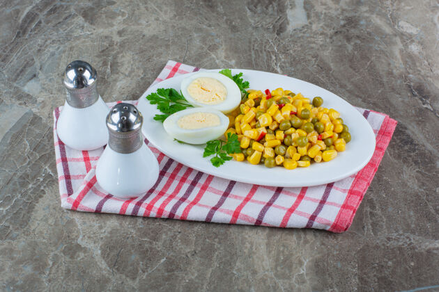茶巾玉米沙拉和鸡蛋片放在盘子旁边 盐放在茶巾上 大理石上美味可口胡椒