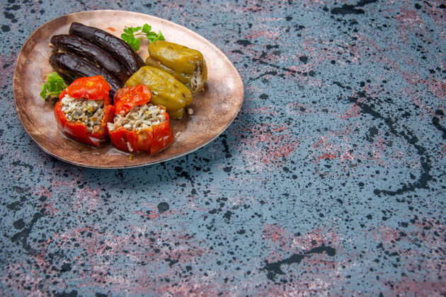 背景前视图茄子与煮熟的西红柿和甜椒与肉末填充在蓝色背景板内多尔玛番茄菜晚餐