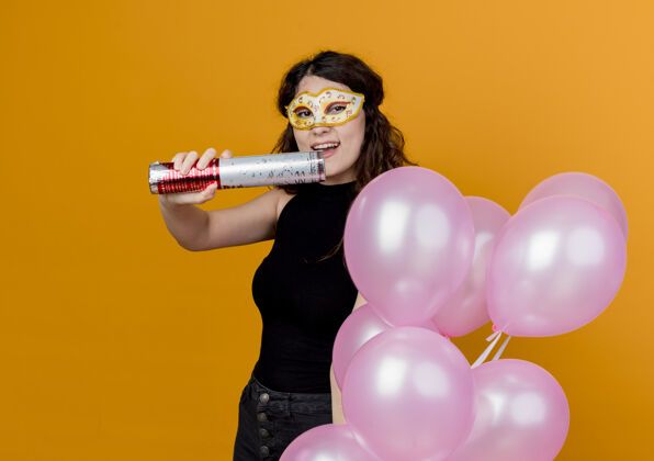 束年轻漂亮的女人卷发手持一束气球在派对面具快乐快乐的生日派对概念超过橙色女人头发面具