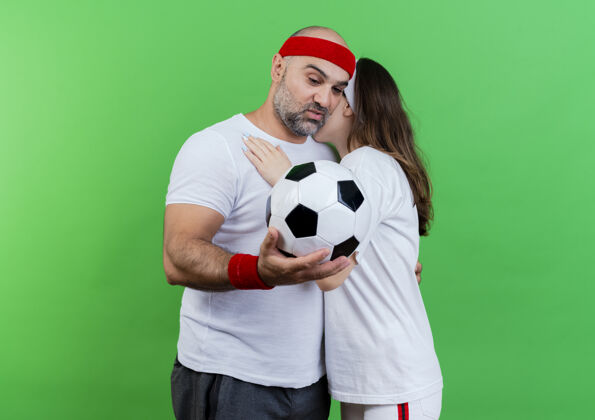 球一对戴着头带和腕带的成年运动型情侣相互拥抱 给手持和看着足球的男人留下了深刻的印象腕带抱着看