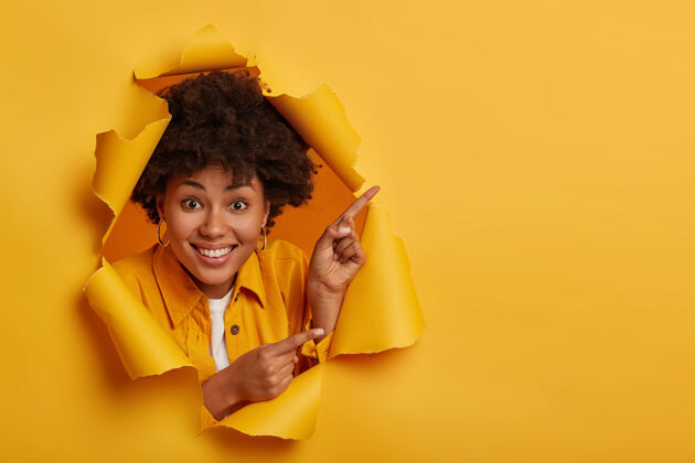 洞积极的美国黑人女士展示了一些惊人的东西 用食指向上和侧面指 广告复制空间 有牙齿的微笑 隔离在黄色背景下欢呼撕扯情绪
